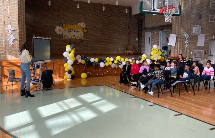  Students sitting in a gym with a teacher by a smart board
